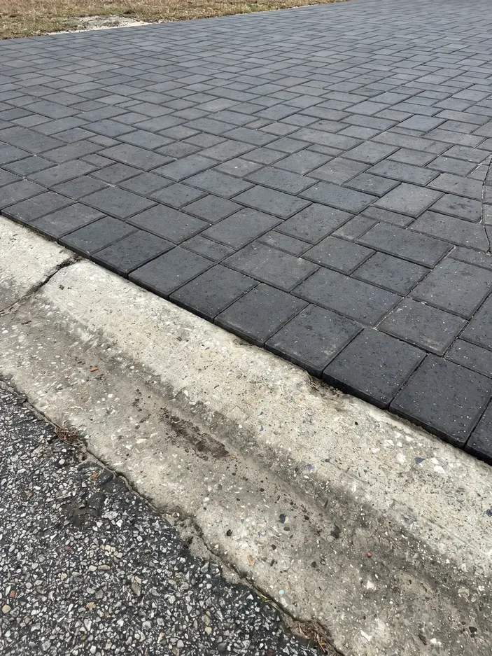 A charcoal paver driveway meeting the street gutter