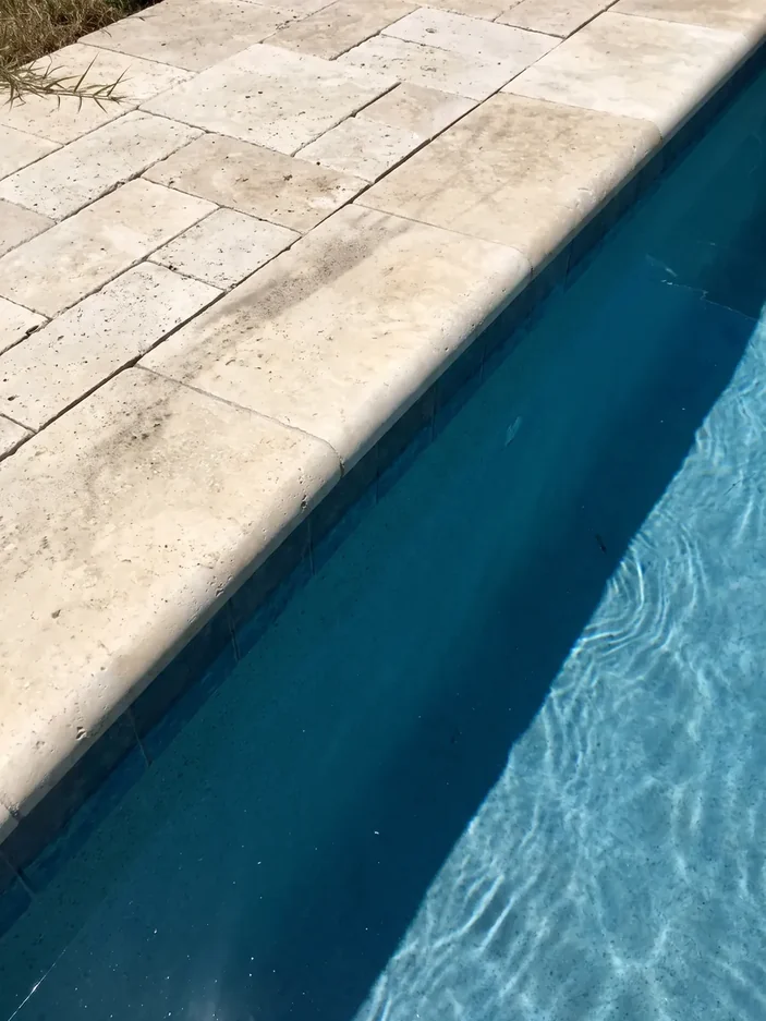 The bullnose coping of a travertine pool deck at the water's edge