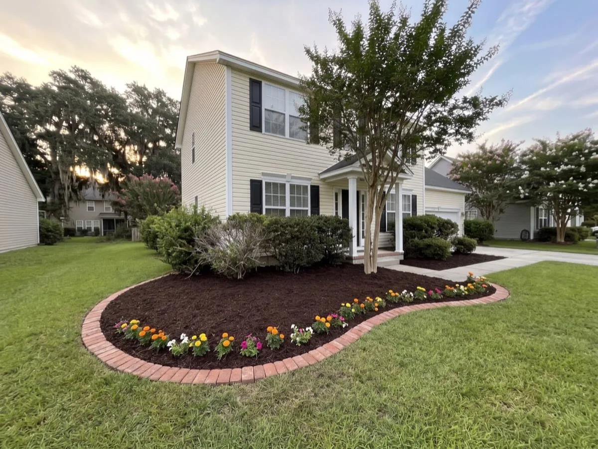 A curved bed in fresh mulch with a brick edge and new plants