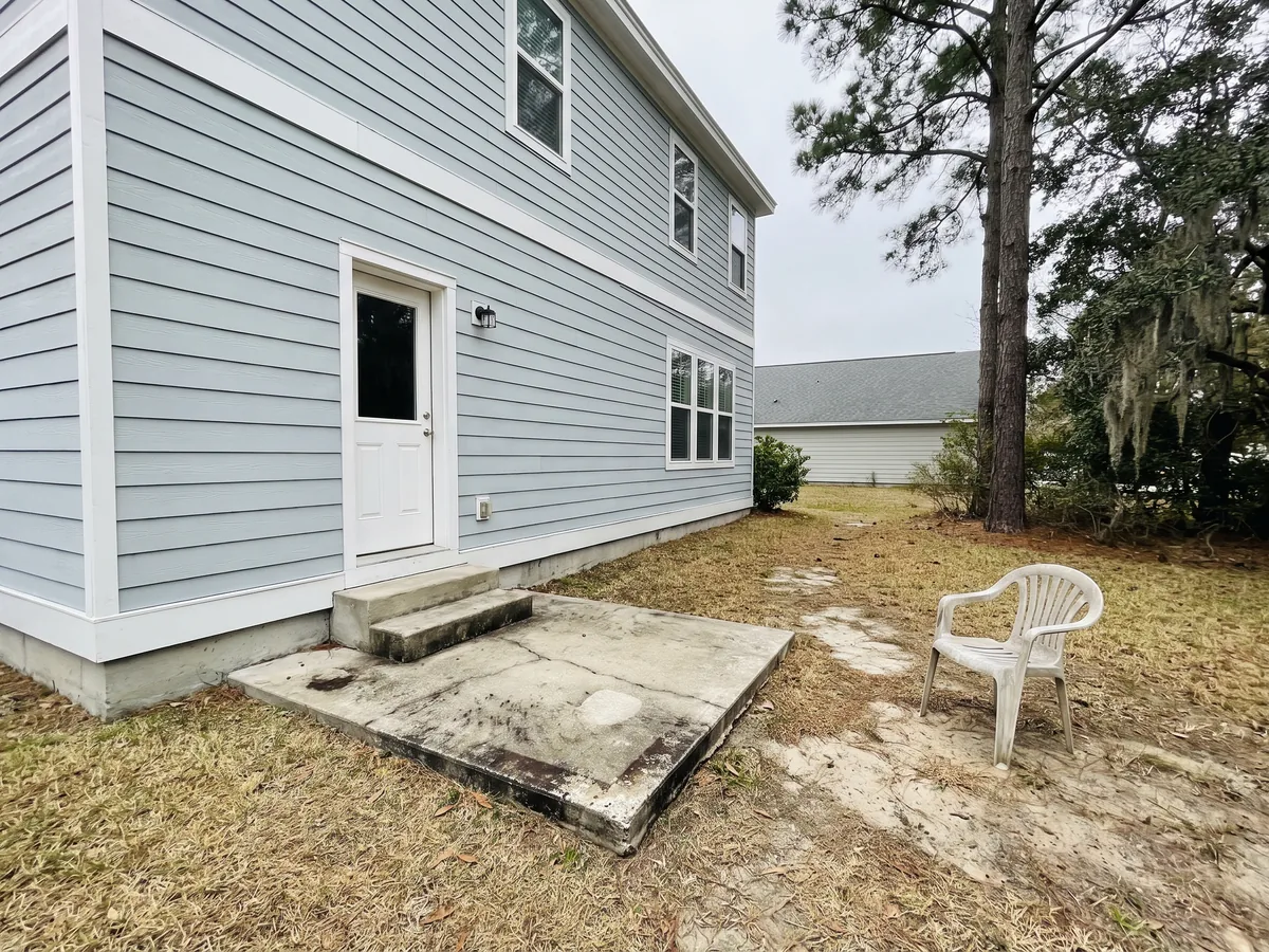 Before: The back of a blue-gray house with a small cracked concrete stoop and a worn dirt path in thin grass